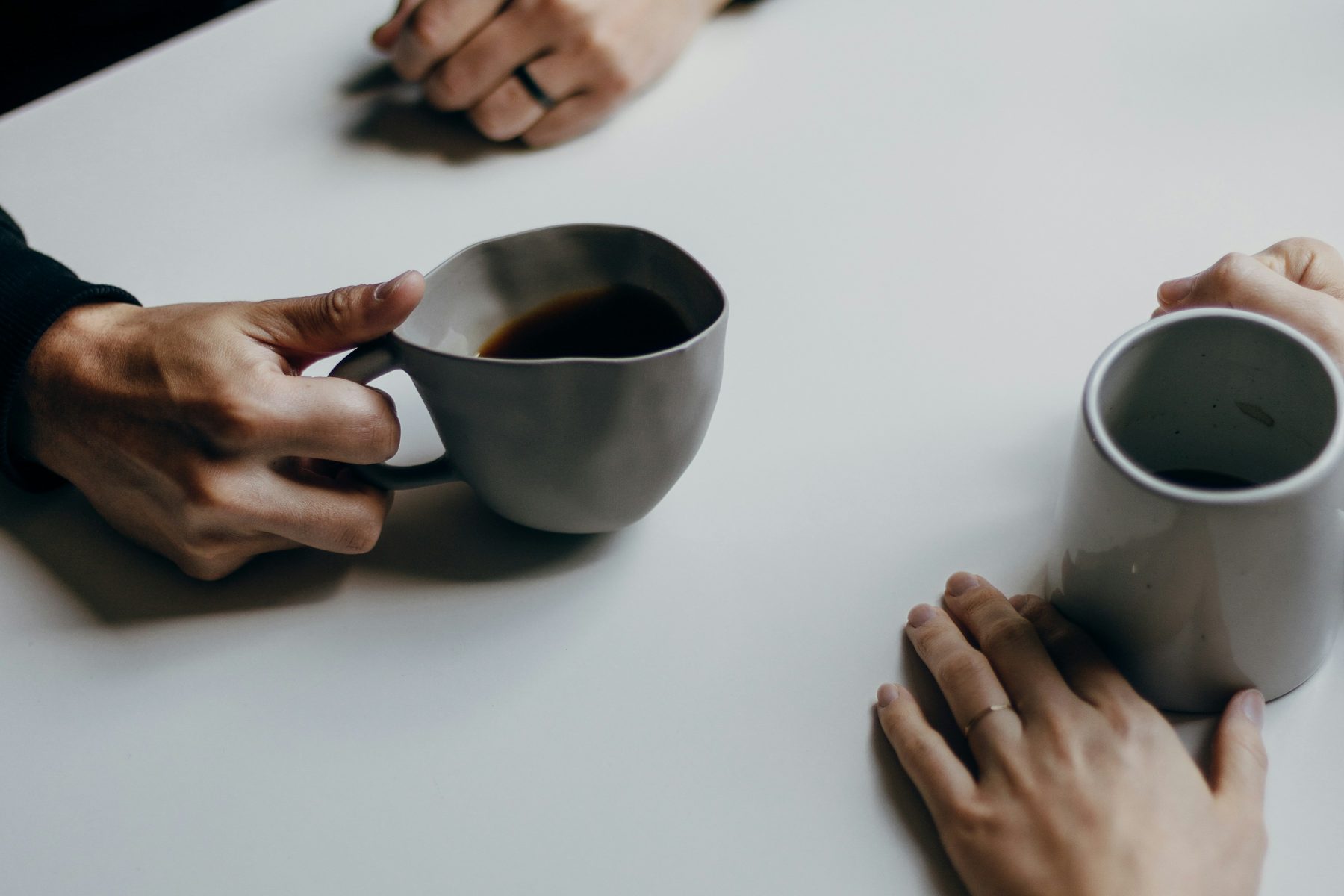 Two people sitting across a table with mugs, hands resting on the table