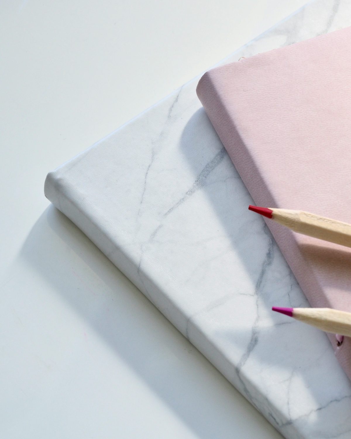 A marble-covered journal and a pink journal stacked together with two colored pencils