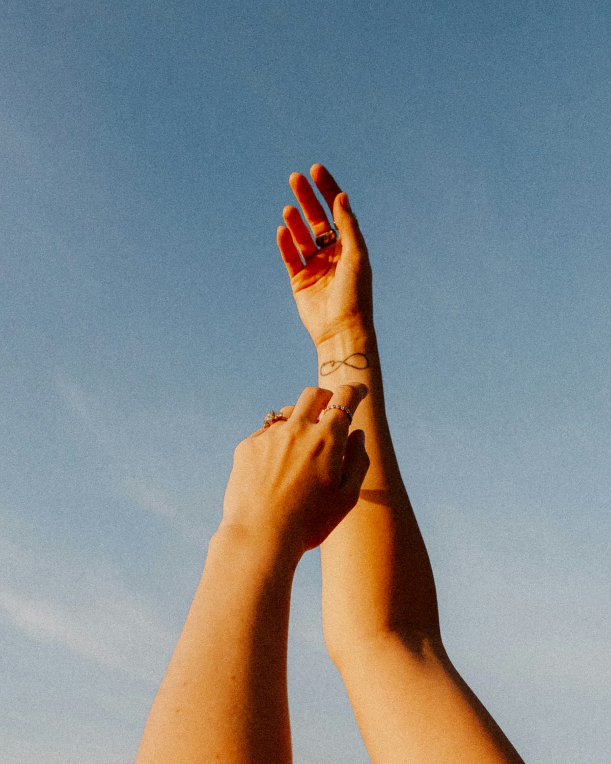 Two raised arms reaching toward a clear blue sky
