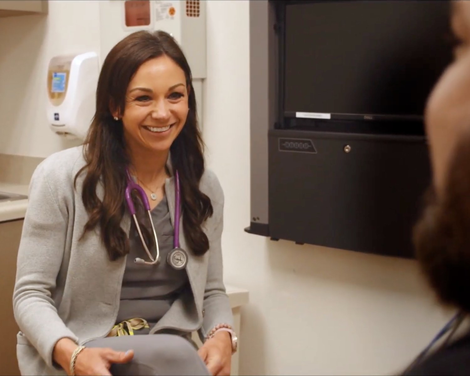 Emily Ray, DO smiling and talking with a patient in an exam room, stethoscope around her neck